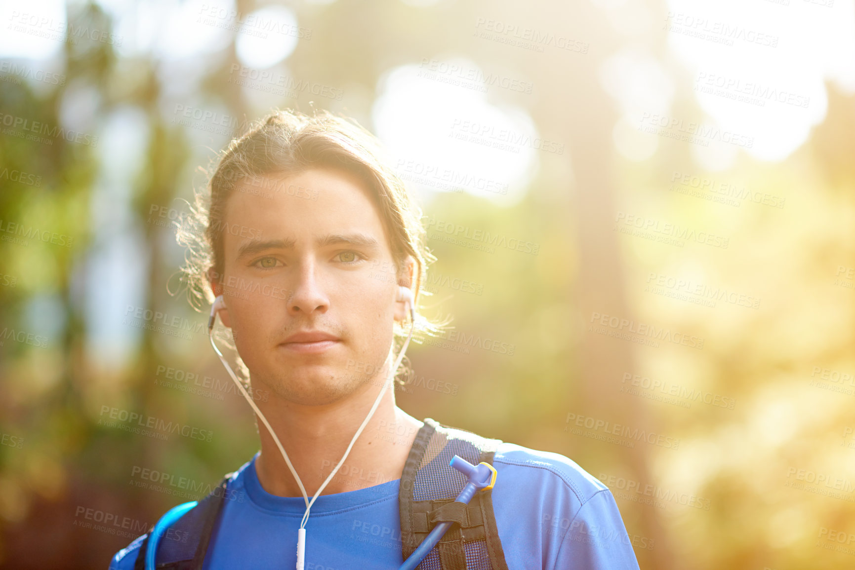 Buy stock photo Fitness, man and portrait with earphones in forest for running podcast, cardio playlist or marathon training. Sunlight, space or trail runner with backpack in woods for wellness or listening to radio
