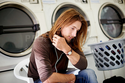 Buy stock photo Man, earphones and listening with music in laundromat for audio streaming, sound or playlist. Male person, break or customer waiting with basket, laundry or online podcast for dry cleaning or washing