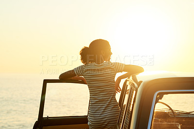 Buy stock photo Shot of a young woman watching the sun go down on a roadtrip