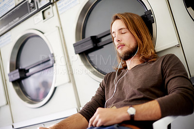 Buy stock photo Man, earphones and listening to music in laundromat for audio streaming, waiting or chill at washing store. Male person, sound or relax with playlist for break, rest or online podcast at laundry shop