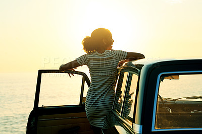 Buy stock photo Shot of a young woman watching the sun go down on a roadtrip