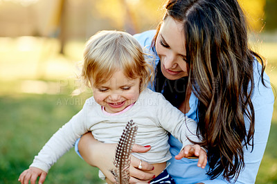 Buy stock photo Outdoor, mother and girl with feather, smile and bonding together with happiness. Family, parent and mama in park, daughter and childhood with weekend break, curious and kid with fun and playing