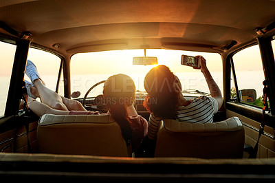 Buy stock photo Shot of two young women taking selfies with a mobile phone on a road trip