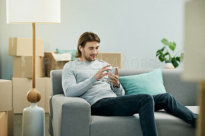 Buy stock photo Man, phone and boxes in new home, couch and listen to music with earphones, texting or web chat in lounge. Person, smartphone and scroll with mobile app, streaming subscription and audio at apartment