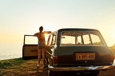 Buy stock photo Shot of a young woman watching the sun go down on a roadtrip