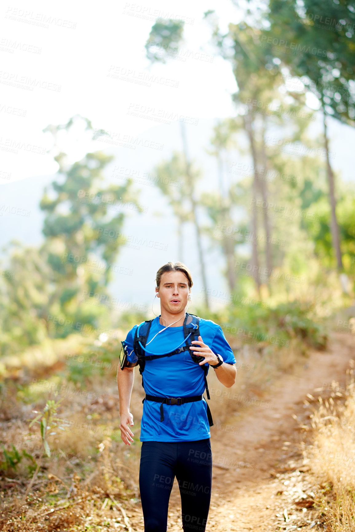 Buy stock photo Fitness, man and running in nature for training, cardio exercise or challenge with music. Runner, earphones or workout on forest trail with motivational podcast, wellness or intense breathing on path