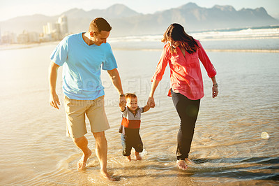 Buy stock photo Happy family, holding hands or walking with baby on beach for holiday, weekend or bonding in nature. Mom, dad and playing with toddler in water for fun summer vacation or outdoor getaway together