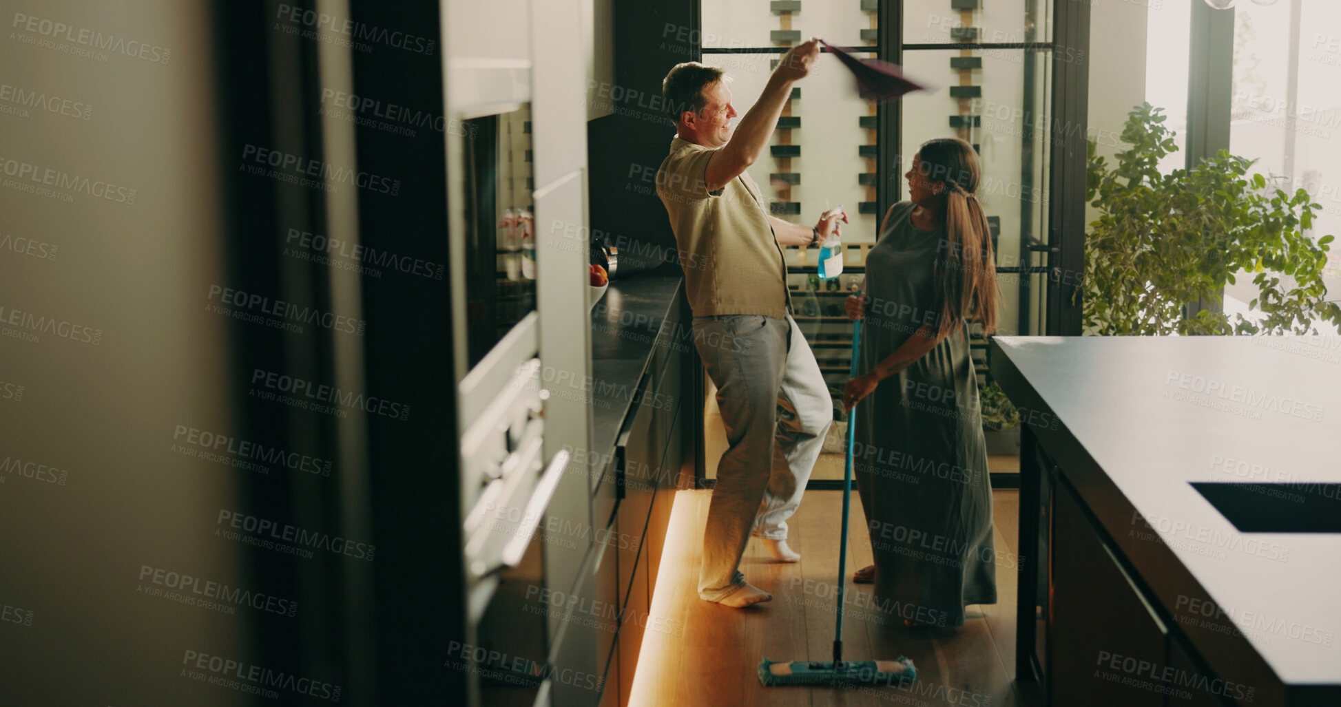 Buy stock photo Happy, couple and cleaning in kitchen with dance, feel good energy and maintenance for hygiene. People, interracial marriage and fun movement in home with household chores, productivity and bonding.