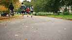 A diverse group of people completing a cardio workout and running through a park together. Back of a group of friends jogging through a garden together. Friends training together running on a park