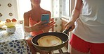 A woman flipping a pancake while her friend takes a photo on her cellphone