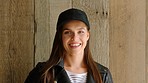 A young woman wearing a trendy hat posing and smiling in front of a wood wall. A cheerful, carefree young woman laughing while posing by a wooden wall wearing a fashionable hat