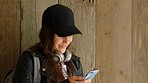 A happy young woman reading texts on her cellphone and smiling before going to university. A young woman on a holiday smiling while using her smartphone to send text messages standing by a wood wall