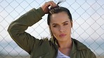 A young woman on holiday untying her hair and standing in front of a fence. A young woman standing by a fence removing her hair tie and shaking out her hair