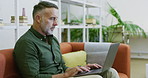 Mature businessman using a laptop to search the internet in an office. Smiling confident creative professional sitting and using technology to research a strategy. Happy designer thinking and planning