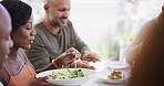 Diverse group of cheerful best friends eating feast and drinking wine while having lunch party around a table in restaurant or home. Happy men and women dishing food while socializing over a meal