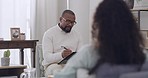 African american male psychologist making notes while listening to his female patient talk about her issues and emotions. Young patient talking to her shrink during a therapy session
