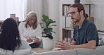 Young interracial couple arguing during therapy session with their mature female therapist in a office while sitting on a sofa. Unhappy boyfriend and girlfriend trying to resolve relationship issues