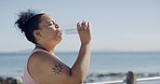 Plus size woman drinking water from bottle after running outside. Chubby active latino taking break to hydrate, refresh. Getting fit, staying healthy and losing fat in routine weight control workout