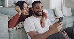 Young mixed race couple relaxing on the sofa in the lounge and using a smartphone while laughing and being affectionate. Hispanic man and woman smiling and enjoying bonding at home