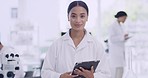 Portrait of a young scientist using a digital tablet on blur background in a lab with coworkers. Confident African biologist working on research using modern technology at medical science laboratory