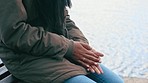 Closeup of hands rubbing together in cold winter. Anxious female nervously thinking about her problems. Woman in a jacket warming her fingers on a freezing day outside, sitting on a bench by the sea.