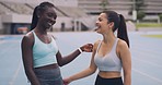 Two supportive female athletes talking and hugging at a sports ground. Portrait of athletic fit sportswomen meeting at a stadium. Active friends embracing and hugging outdoors after exercising