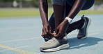 Closeup of an African female athlete tying shoe laces before jogging. Active fit woman ready and preparing to run on a sports track. Athletic person fasting shoestrings before training and exercising