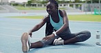 Fit woman stretching her legs and touching her feet for a warmup to prevent injury on a sports track. Happy young african american athlete preparing her body and muscles for a cardio training workout