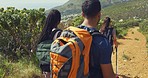 Diverse hikers wearing backpacks while trekking on a mountain trail. Group of young friends out hiking together on a sunny day. Adventurous backpackers out exploring nature and spending time together