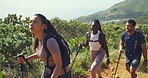Diverse group hiking on a mountain path for fitness on a sunny day. Three active people backpacking on rocky trail with walking sticks. Two women and a man on an adventure, enjoying exploring nature