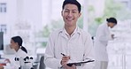 Portrait of a young male scientist with a clipboard on blur background in a lab with coworkers. Happy biologist analyzing research report and writing on a checklist at a medical science laboratory