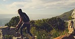 Fit active woman hiking on a mountain using a binocular. Hiker wearing a backpack standing on the edge of a cliff and looking at the landscape with a sunset and ocean in the background on a windy day