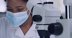 Female scientist using a microscope and a mask in a research lab. Young biologist or biotechnology researcher working and analyzing microscopic samples with the latest laboratory tech equipment