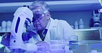 Mature medical scientist using microscope to examine monkeypox or corona virus samples in ultraviolet lit lab. Male Biochemist, genetic engineer or doctor doing medical research in science facility