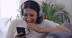 Woman laughing watching funny videos online with her phone at home. Female streaming series and chatting with friends on social media. Girl smiling while sending text message and listening to podcast