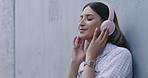 Woman listening to music on bluetooth headphones, leaning against a concrete wall outside and dancing. Young female enjoying playlist of her favorite songs on wireless audio equipment in the city