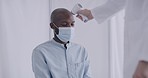 A male doctor taking measures a patient’s temperature using a non-contact infrared thermometer in an apartment, a man wearing the mask, of an African person. Doctor giving the report on COVID-19.