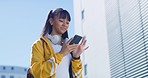 A beautiful young woman with white stylish headphones around her neck, standing in the background of the city square and using a smartphone. A girl using a GPS location app on the mobile phone.