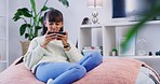 Teenager using a phone while relaxing on a bean bag in the living room at home. Young girl playing a mobile game or streaming a video on the weekend. Enjoying free time on internet or social media 