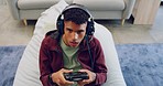 A young gamer talking on a wireless headset while sitting on a couch and playing a console video game. Using a controller to play multiplayer online and having fun while looking serious and focused