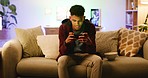 A young confident male gamer playing a mobile game on his phone and talking. Handsome guy streaming video games and sitting on a sofa at home. One man gaming on the weekend or in the evening 