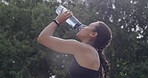 A female athlete drinking water after an exercise outdoors in a park with copy space. A young athletic and active woman hydrating after a workout. Fit sports person refreshing after running