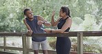 Two fit athletes doing a high five on a bridge in a park on a summer day. Young healthy couple taking photos while training together outside. Focused couple getting a cardio workout in nature