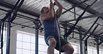 Fit and sporty young man exercising on a climbing rope during his workout at the gym. Dedicated sportsman strengthening his core and building strong muscles in a workout and fitness facility