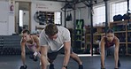 Active people using dumbbells for plank and renegade rows while training in a gym. Group of focused and diverse athletes exercising with heavy weights to gain muscle and endurance in a fitness class