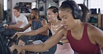 Fit people using air bikes for cardio exercise in gym. Diverse group of athletic, healthy men and women listening to music on earphones or headphones. A sweaty workout and training class with friends