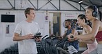 Gym instructor giving thumbs up to trainees and using digital tablet to check their workout stats. Male trainer encouraging young sport clients and monitoring their progress during endurance training