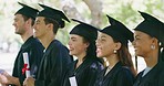 Group of university or college graduates in mortarboards and gowns standing in a line at their graduation ceremony outside. Proud students holding their degrees or diplomas after educational success