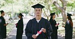 Portrait of a confident male graduate at a university or college campus holding his degree. A young male who received his honors or diploma at a graduation ceremony standing with his classmates