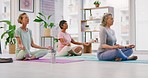 Mature women meditating in lotus pose with mudra hand gesture during a fitness class in a yoga studio. Calm, relaxed and focused ladies sitting and praying quietly for inner peace and zen energy